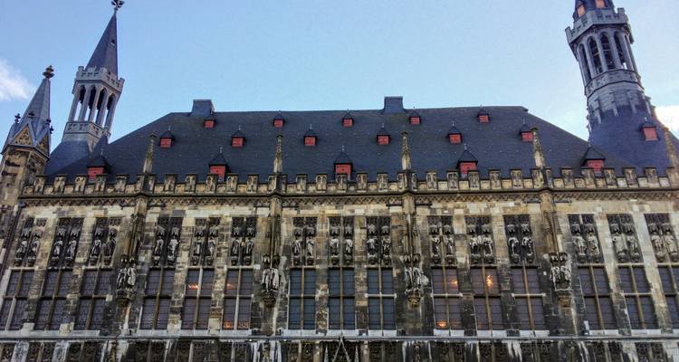 Façade avant de l'hôtel de ville d'Aix-la-Chapelle avec rangées de statues gothiques et lucarnes rouges.