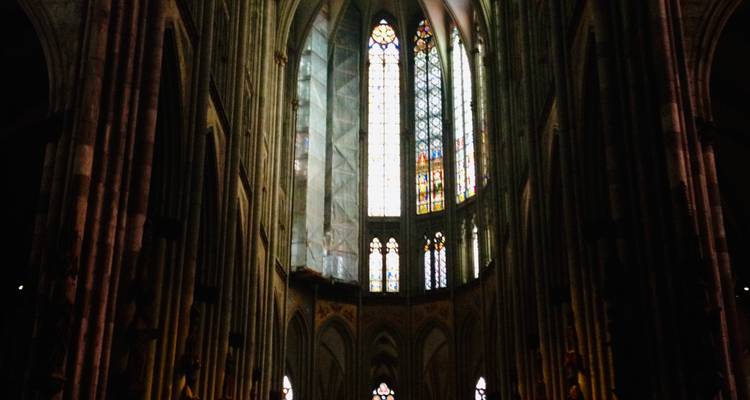 Nef intérieure sombre de la Cathédrale de Cologne avec des colonnes élancées et de hautes fenêtres en vitrail.