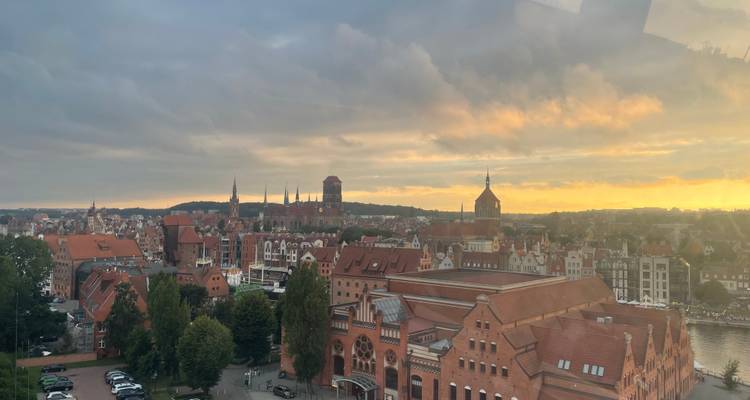 La lumière dorée du coucher de soleil illuminant la ligne d'horizon aux toits rouges de Gdańsk avec des nuages dramatiques.
