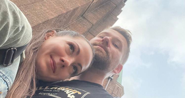 Selfie en gros plan vers le haut d'un couple s'embrassant avec une haute tour d'église en brique en arrière-plan.
