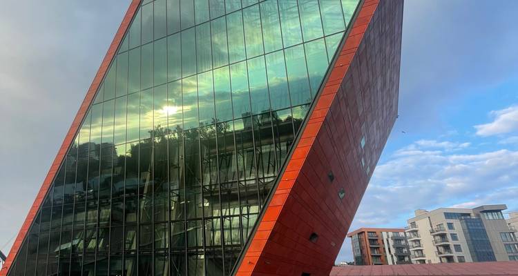 Musée en verre vêtu de rouge moderne et incliné reflétant le ciel au coucher du soleil.