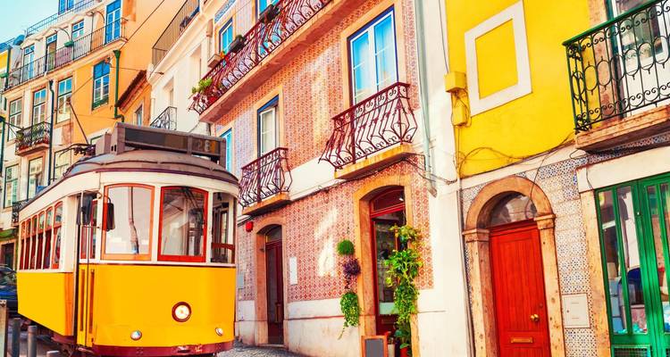 Un tramway vintage jaune éclatant passe devant des immeubles aux carrelages colorés dans une rue ensoleillée de Lisbonne.