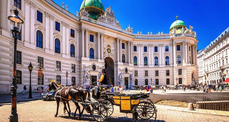 Un fiacre passe devant la façade baroque ornée et les dômes verts du Palais de la Hofburg de Vienne par une journée ensoleillée.