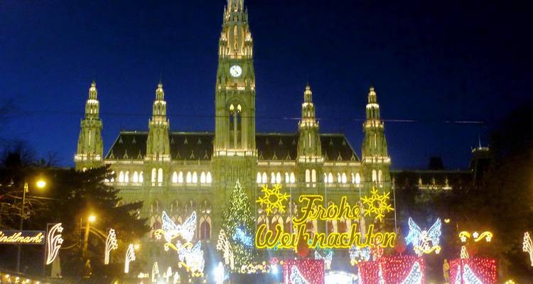 Le Rathaus de Vienne illuminé pour le marché de Noël avec des lumières festives, un sapin et une foule la nuit.