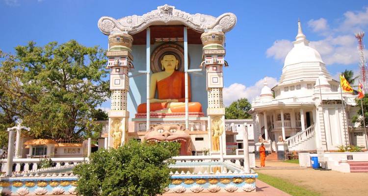 Façade de temple bouddhiste colorée avec une gigantesque peinture de Bouddha assis flanquée de piliers ornés.