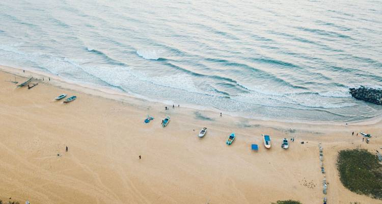 Vue en plongée d'une large plage de sable avec des bateaux éparpillés et de petites vagues qui s'échouent sur le rivage.