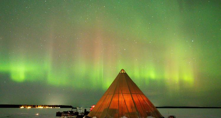 Aurore boréale verte brillant au-dessus d'un tipi couvert de neige dans un paysage gelé.