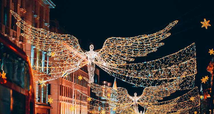 Des installations lumineuses spectaculaires d'anges de Noël s'étendant sur une rue animée de Londres la nuit.