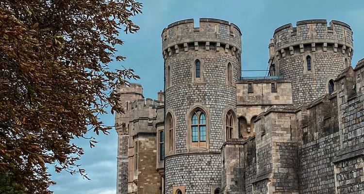 Les tours en pierre et les créneaux d'un château médiéval encadrés par le feuillage automnal sous un ciel bleu.