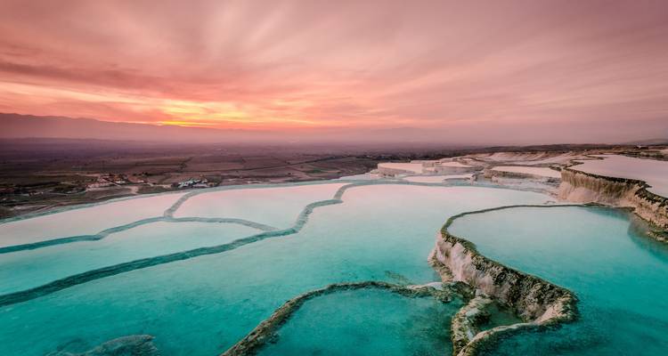 Coucher de soleil sur les terrasses de travertin de Pamukkale remplies de bassins turquoise surplombant de vastes plaines.