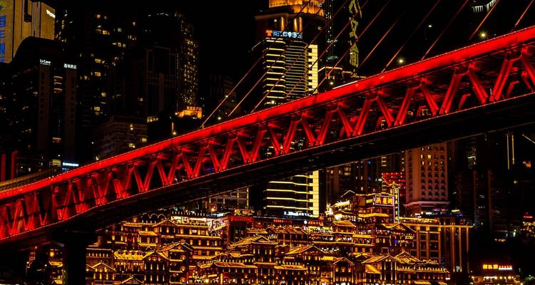 Panorama nocturne de la ligne d'horizon illuminée de Chongqing avec le spectaculaire pont rouge Qiansimen en premier plan.