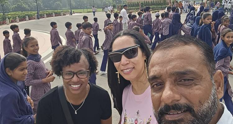 Selfie de deux touristes avec leur guide devant un grand groupe d'écoliers en uniforme en Inde.