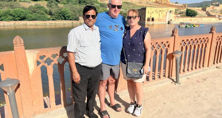 Un guide touristique et un couple posent à côté d'un lac avec le Fort d'Amber de Jaipur en arrière-plan.