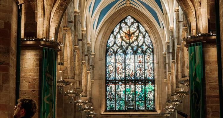 Interior de iglesia gótica impresionante con columnas elevadas y ventana de vidriera de colores que captura la luz filtrada.