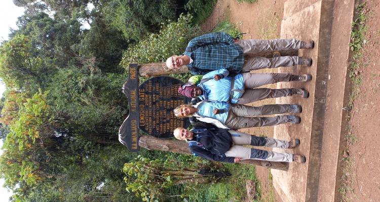 Une petite équipe de trekkeurs se tient près du panneau en bois de la porte de Lemosho à l'entrée du sentier du parc national du Kilimandjaro.