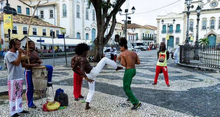 Straßenkünstler üben Capoeira mit Trommeln und hohen Tritten auf einem Kolonialplatz.