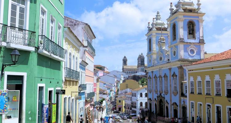 Pastellfarbene Fassaden und eine barocke blaue Kirche überblicken eine lebhafte Straße in Salvador.
