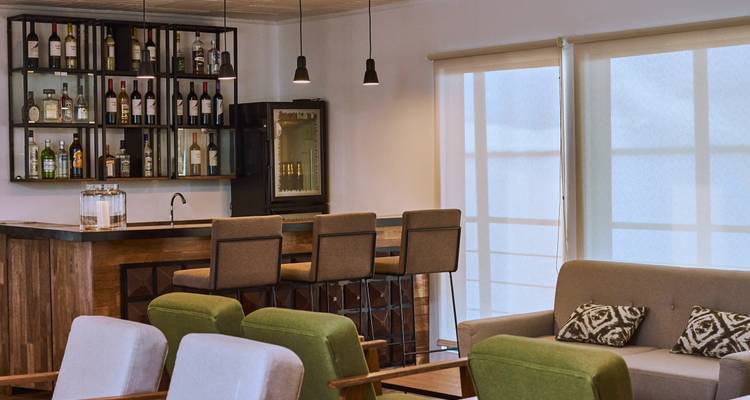 Zone de détente et bar accueillante avec des fauteuils verts et un mur de spiritueux en bouteille à bord d'un navire fluvial.