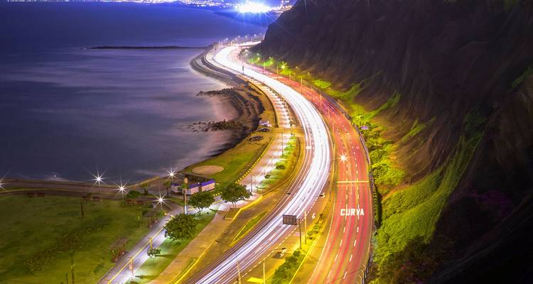 Foto de larga exposición nocturna de la carretera costera de Miraflores con brillantes rastros de luz blanca y roja junto al Océano Pacífico.