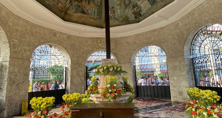 Intérieur du pavillon de la Croix de Magellan orné de peintures murales et d'arrangements floraux frais tandis que les visiteurs se rassemblent à l'extérieur.