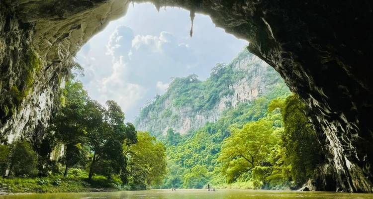 La vista desde adentro de una caverna revela bosques esmeraldas y acantilados de piedra caliza enmarcados por el arco irregular de la cueva.