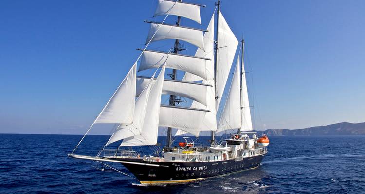 Élégant grand voilier aux voiles blanches complètes fendant les eaux bleu profond de la mer Égée sous un ciel dégagé.