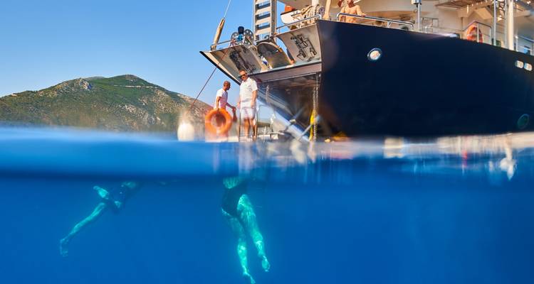 Image en deux niveaux montrant des nageurs sous l'eau bleue scintillante tandis que les membres de l'équipage se tiennent sur la plateforme de baignade du yacht.