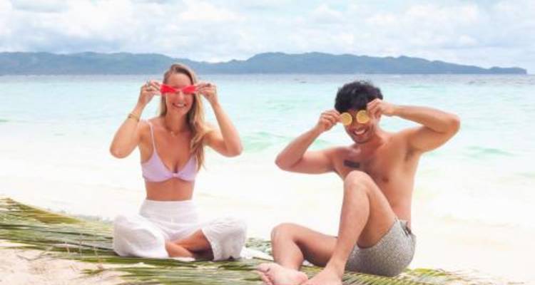 Couple souriant jouant avec des tranches de fruits sur une plage tropicale aux sables blancs