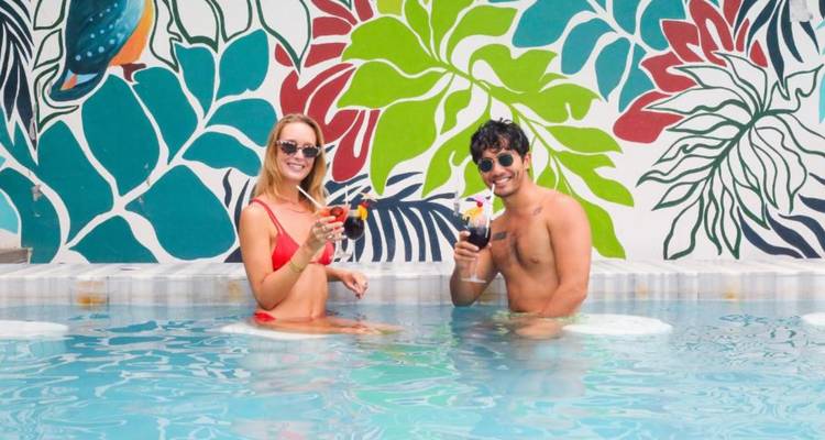 Couple portant un toast avec des cocktails colorés dans une piscine plongeante encadrée de fresques murales