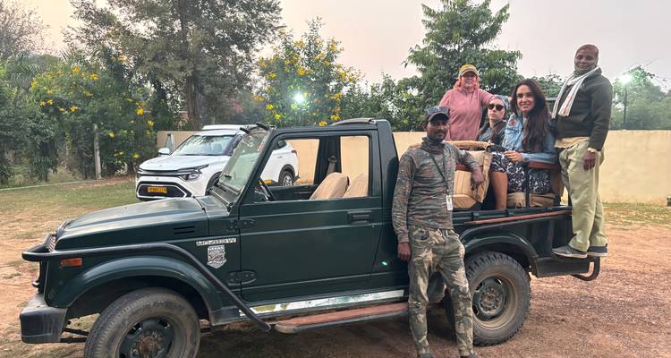 L'équipe de safari se tient à côté d'un véhicule tout-terrain à hayon ouvert vert foncé au crépuscule dans un camp de base.