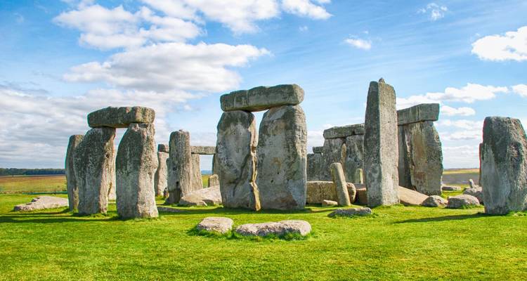 Le cercle de pierres emblématique de Stonehenge se dresse sur un terrain herbeux ouvert sous des nuages épars.