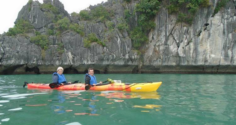 Dos viajeros en un kayak tándem se deslizan junto a acantilados de piedra caliza imponentes sobre aguas de jade en la Bahía de Lan Ha.