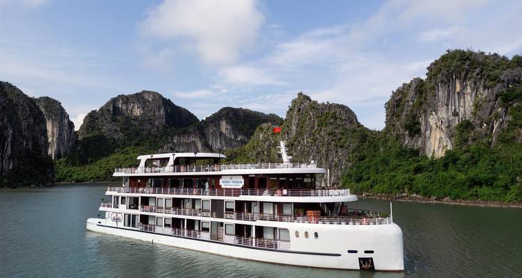 Un crucero de lujo blanco navegando entre imponentes formaciones de piedra caliza en las aguas de color esmeralda de la Bahía de Halong.