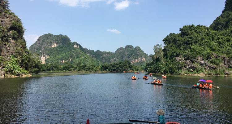 Los botes de remos con turistas se deslizan por un río tranquilo rodeado de exuberantes picos de piedra caliza en el campo de Ninh Binh.