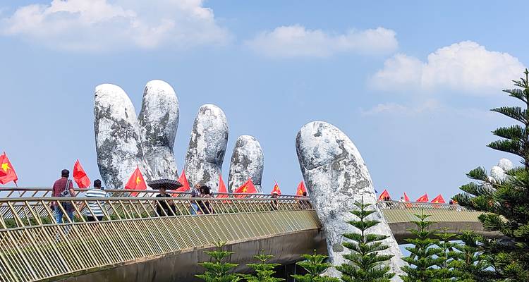 Los visitantes caminan por el dramático Puente Dorado sostenido por enormes manos de piedra contra el cielo azul en Da Nang.