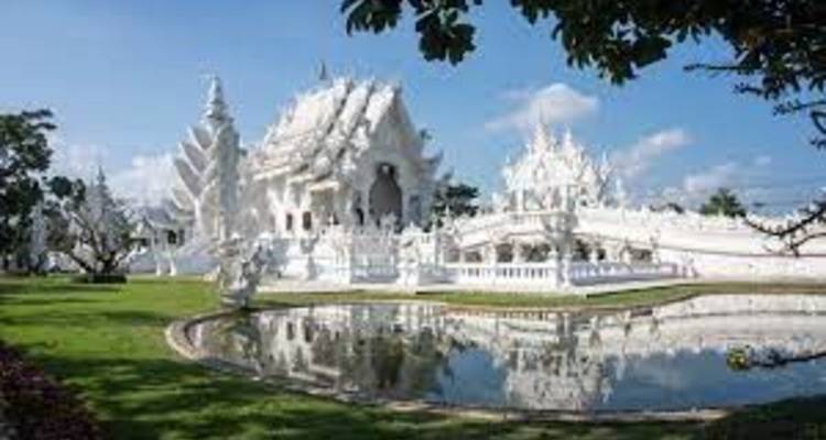 Blendend weißer Tempelkomplex Wat Rong Khun, der sich an einem sonnigen Tag in einem kleinen Teich spiegelt.