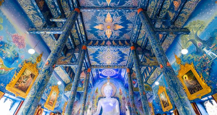 Lebendiges blaues Interieur des Wat Rong Suea Ten mit aufwendigen himmlischen Wandmalereien und einer weißen Buddha-Statue