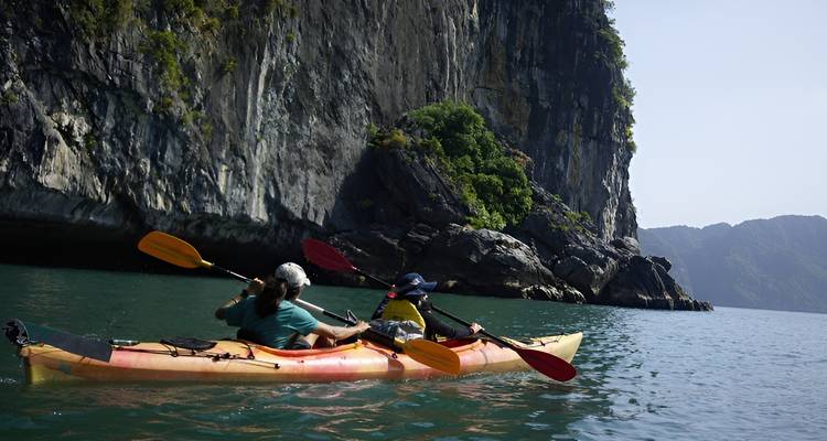 Pareja de kayakistas remando cerca de acantilados de piedra caliza imponentes sobre agua azul-verdosa cristalina