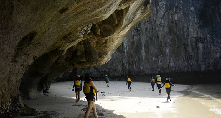 Aventureros con chalecos salvavidas explorando una cala arenosa bajo un saliente rocoso
