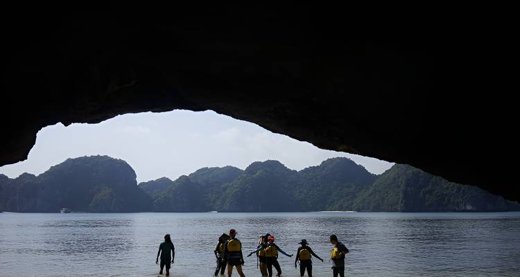 Grupo silueteado enmarcado por la boca de la cueva, mirando hacia la bahía tranquila y los picos boscosos