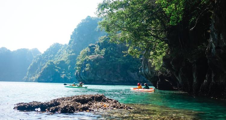 Kayakistas remando frente a acantilados de karst exuberantes en aguas esmeralda cristalinas