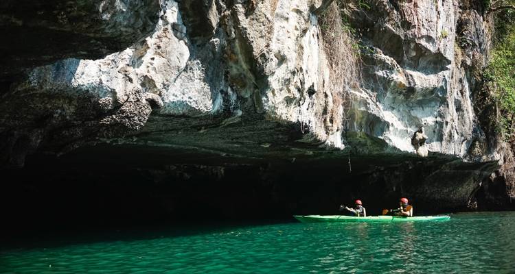 Dos kayakistas entrando a una cueva de piedra caliza oscura sobre aguas verde profundo