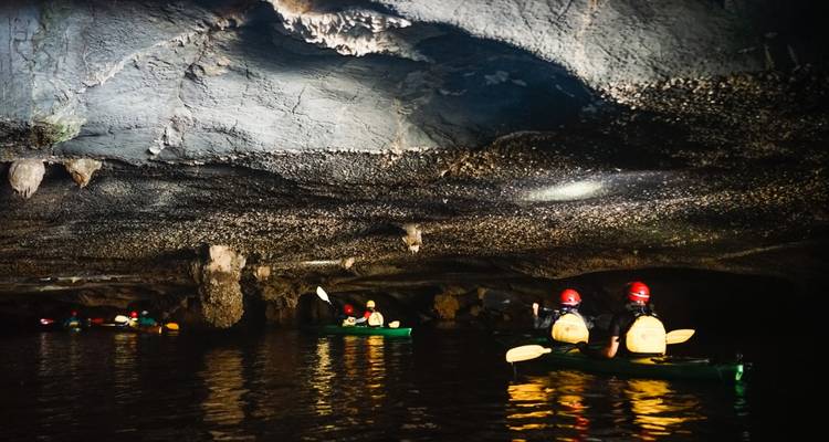 Grupo de kayakistas con linternas frontales remando a través de una cueva de agua oscura