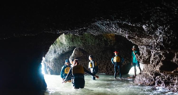 Exploradores de pie en agua hasta las rodillas dentro de una rústica cueva marina iluminada desde afuera