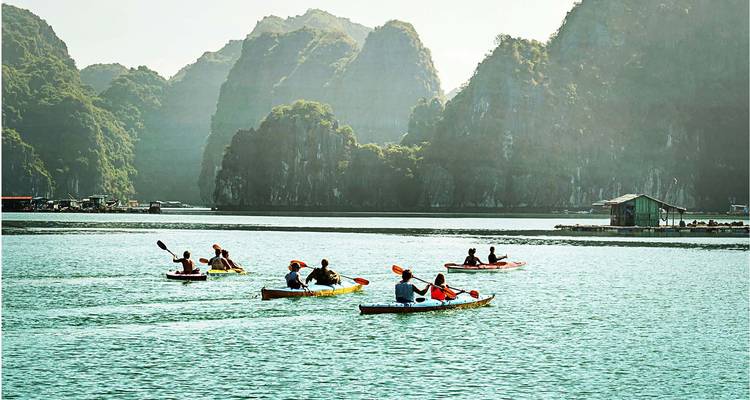Varios kayaks con remeros deslizándose sobre aguas turquesas con un telón de fondo de islas de piedra caliza envueltas en neblina.