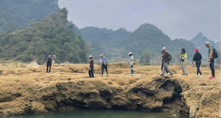 Senderistas cruzando una formación de puente de piedra caliza rocosa sobre una pequeña piscina en un paisaje kárstico brumoso.