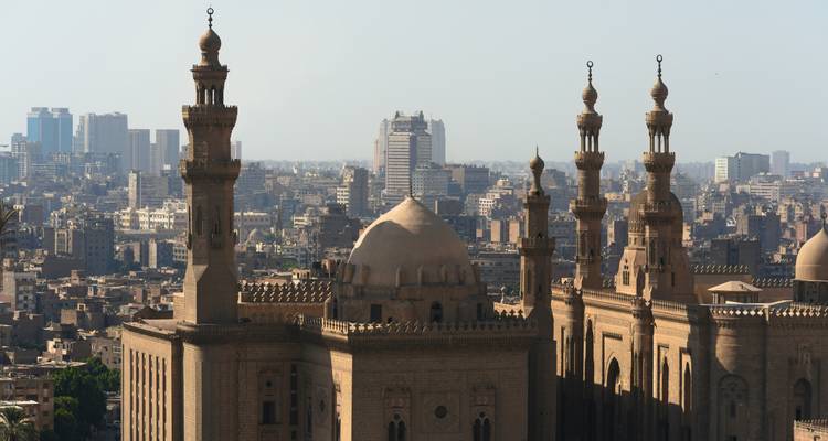 Les mosquées historiques aux minaret ornés s'élèvent au-dessus de l'horizon urbain du Caire avec des gratte-ciel modernes en arrière-plan.