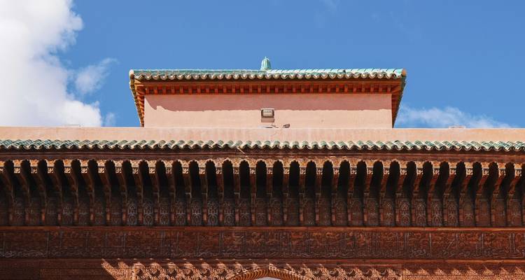 Gros plan sur les corniches en cèdre ouvragé et le toit aux tuiles vertes sur fond de ciel bleu éclatant de Marrakech.