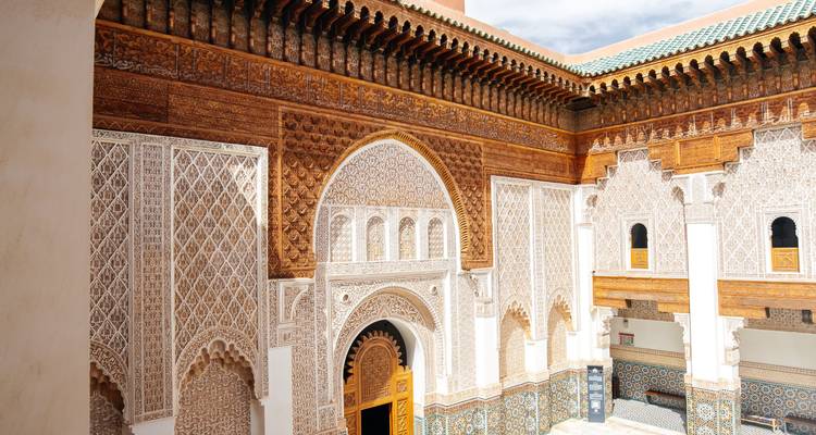 Cour finement sculptée et carrelée de la Médersa Ben Youssef illuminée par le soleil de midi.
