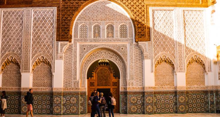 Des visiteurs discutant devant l'arc d'entrée orné d'une médersa historique à Marrakech.